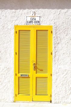 a yellow door is in front of a white building with shutters and a sign above it