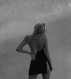 a woman standing in front of a wall with her back to the camera and braided hair