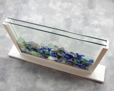 a glass display case filled with lots of blue and green sea glass on top of a wooden stand