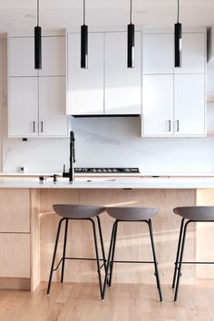 three stools sit in front of an island with white cabinets and countertop space