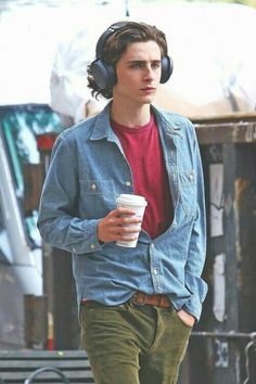 a young man wearing headphones and holding a cup of coffee is walking down the street