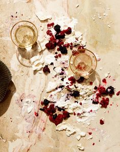 two glasses of wine on a table with food spilled out of the cups and saucers