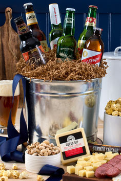 a bucket full of beer and snacks on a table next to other foods, including crackers