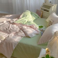 an unmade bed with pink and green sheets on it in front of a window