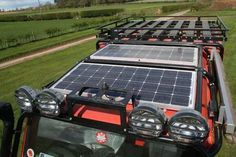 a truck with solar panels on the back driving down a road in front of a green field