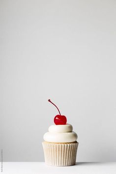 a cupcake with white frosting and a cherry on top by luke van deren for stockstation