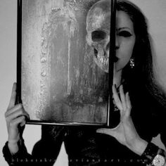 a woman holding up a painting with a skull on it's face in front of her face