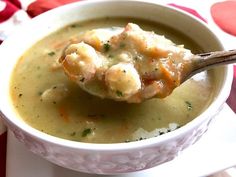 a spoon full of soup with shrimp and cheese in it on a white plate next to a red napkin