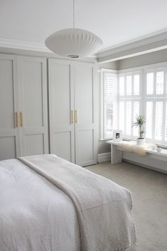 a bedroom with white furniture and large windows in it's center wall, along with a bed on the other side