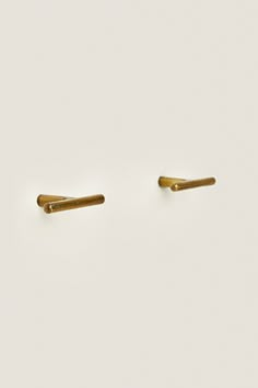 two gold ear pins sitting on top of a white surface with no one in it