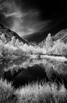 black and white photograph of mountains, water and trees with clouds in the sky above