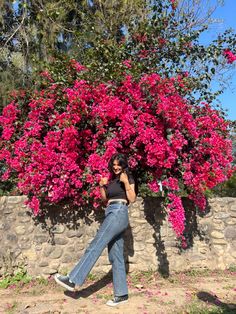 a woman leaning against a stone wall while talking on her cell phone in front of a flowering tree