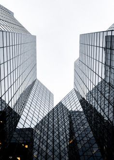 looking up at some very tall buildings with glass windows on each side and the sky in the background