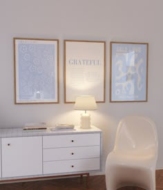 a white chair sitting next to a table with a lamp on it in front of two framed pictures