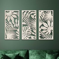 three pieces of paper cut art on a wall in a living room with green couches