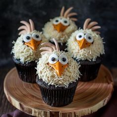 four cupcakes with googly eyes and white frosting on a wooden plate