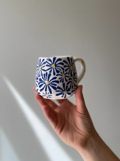 a hand holding a blue and white coffee cup with yellow flowers on the inside, against a white background