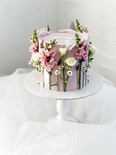 a white cake with pink frosting and flowers on top, sitting on a table