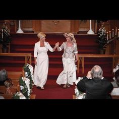 two women in white dresses are walking down the aisle