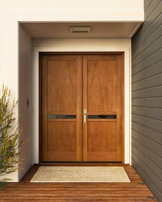 two wooden doors on the side of a house with a rug in front of them