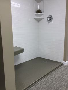 a white tiled shower stall in a bathroom with gray carpeting on the floor and walls