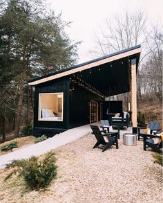 a small black cabin in the woods with patio furniture and lights on it's roof