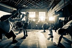 several people are doing exercises in an industrial building with sunlight streaming through the windows and casting shadows on the floor