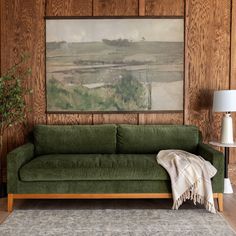 a green couch sitting in front of a painting on the wall next to a lamp