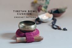 there is a metal bowl sitting on top of some yarns and beads with the words tibetan bowl cushion next to it