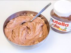 peanut butter in a metal bowl next to a jar of nutella on a white table