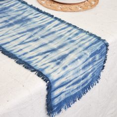 a blue and white tie dyed table runner on top of a dining room table next to a plate