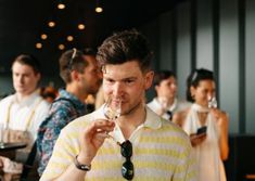 a man holding a wine glass in front of his face while standing next to other people