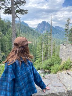 a woman standing on top of a stone wall next to a forest filled with trees