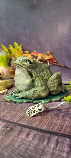 a green frog statue sitting on top of a wooden table next to other items and leaves