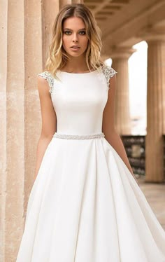 a woman in a white dress standing next to columns and looking down at the camera