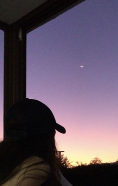 a person sitting in front of a window looking out at the moon and trees outside