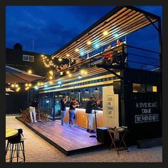 a group of people standing on top of a wooden deck next to a building at night