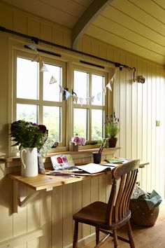 a wooden chair sitting in front of a window next to a desk with flowers on it