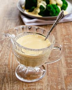 a glass gravy dish with broccoli in the background on a wooden table