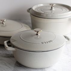 three white pots with lids sitting on top of a marble countertop next to each other