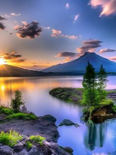 the sun is setting over a lake with mountains in the background and trees on the shore