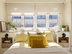 a bed with yellow pillows and white sheets in front of two windows that look out onto the street