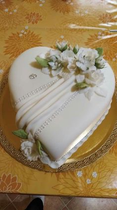 a heart shaped cake decorated with flowers on a gold and white tableclothed table