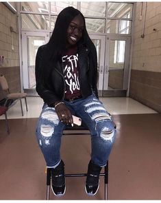 a woman sitting on top of a chair wearing ripped jeans and black boots with her hand in her pocket