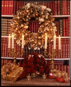 a christmas wreath with candles and presents on a table in front of bookshelves