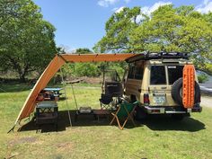 an suv is parked in the grass with its awning open and camping gear set up