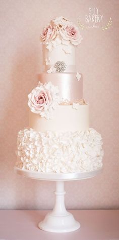 a three tiered wedding cake with pink flowers on top and white icing, sitting on a pedestal