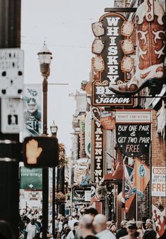 a crowded city street filled with lots of signs and people walking down the side walk