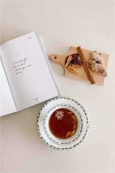 a cup of tea next to an open book on a table with ginger and cinnamon sticks