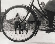 an old black and white photo of a woman standing next to a bicycle wheel with the spokes still in place